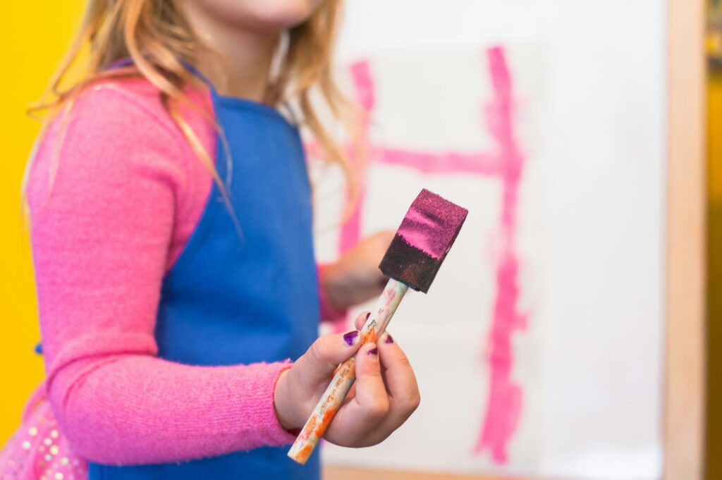 Photo of a child in a pink jumper holding a paintbrush loaded with pink paint